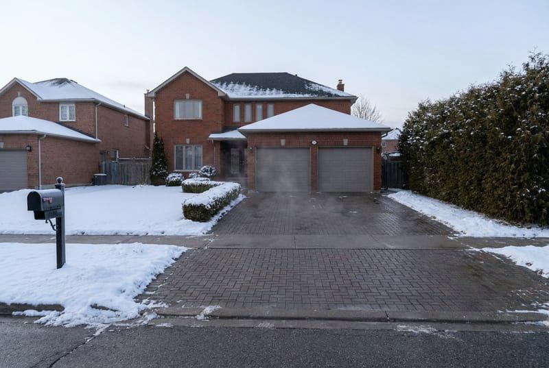 Paver driveway clear of snow in front of a brick house while the lawn stays white